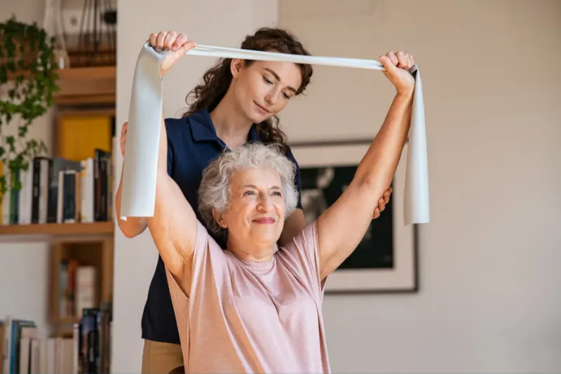 Keeping_your_body_fit1 An older lady stretching/exercising her arms, with a phsiologist helping her