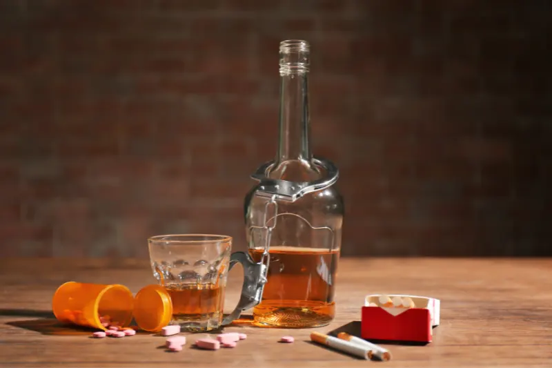 Alcohol_&_drugs1 Alcohol and pills, with a hand cuff around the bottle of alcohol